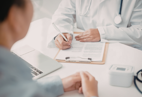 a patient sits at a desk with a doctor as they go through paperwork