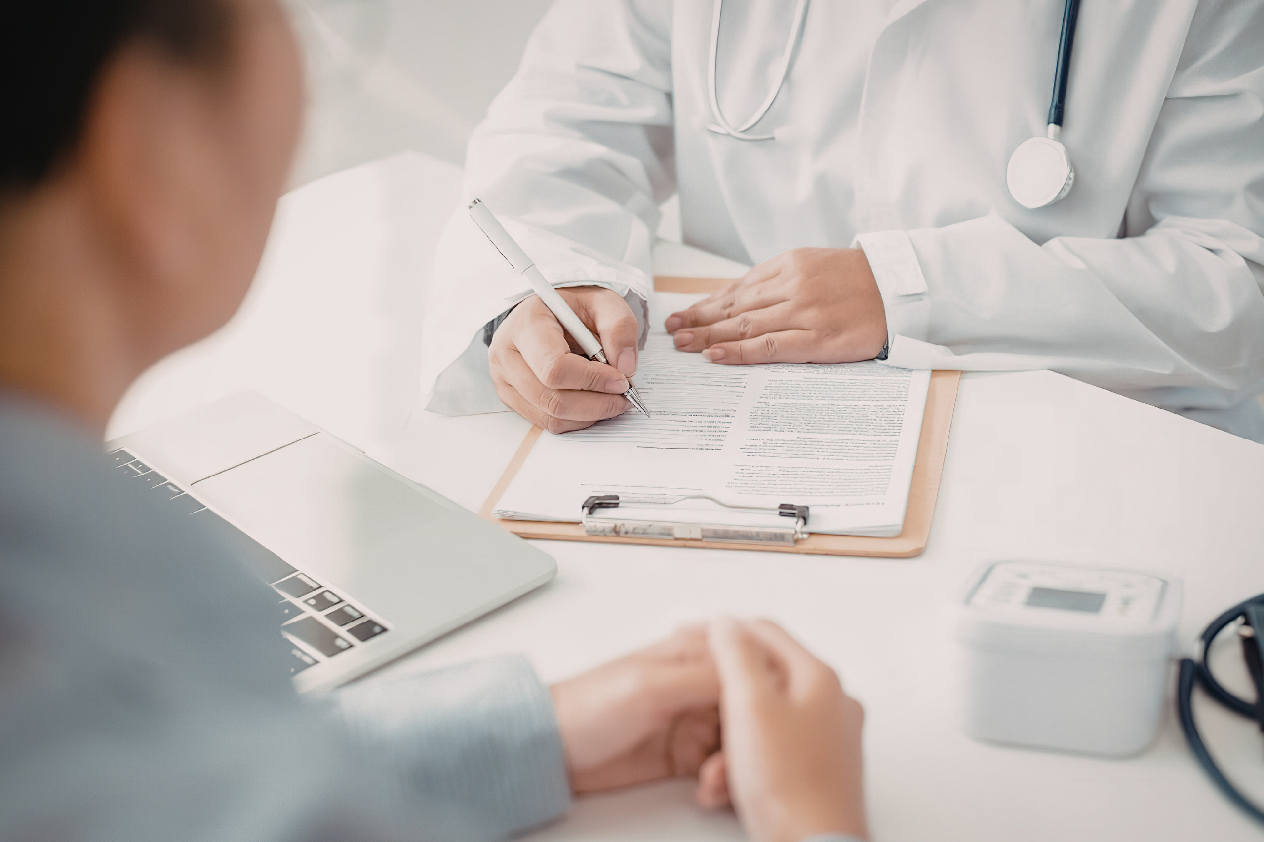 a patient sits at a desk with a doctor as they go through paperwork