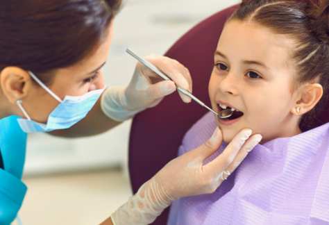 a child sits in a dental chair while a dentist examines their teeth