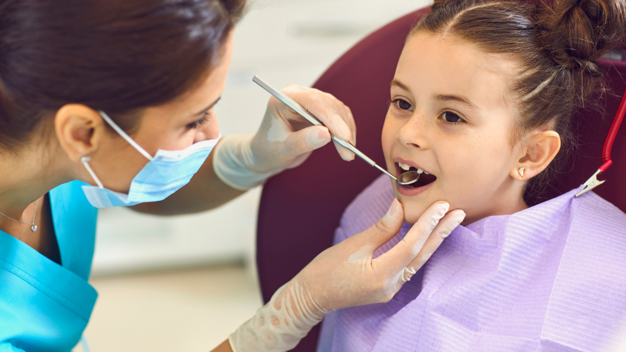 a child sits in a dental chair while a dentist examines their teeth